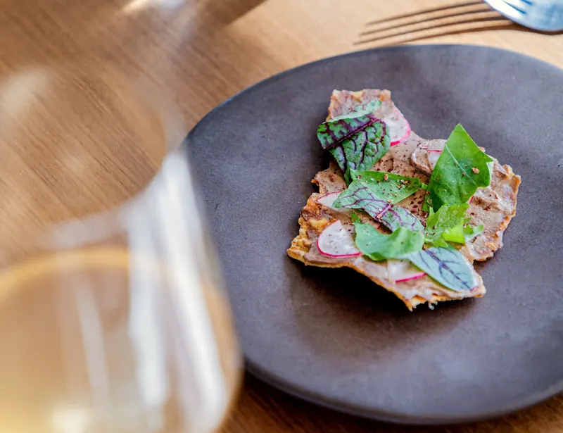 Viande finement tranchée, herbes et radis sur assiette en grès, verre de vin blanc