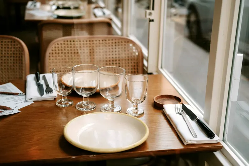 Table en bois dressée près d'une fenêtre, verres, assiette en céramique et serviettes en tissu